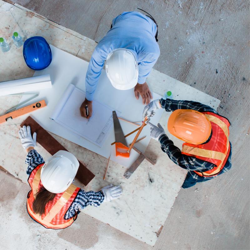 People standing around a table working on architecture with hard hats on