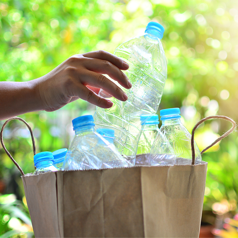 Hand holding a plastic water bottle above a basket of empty bottles