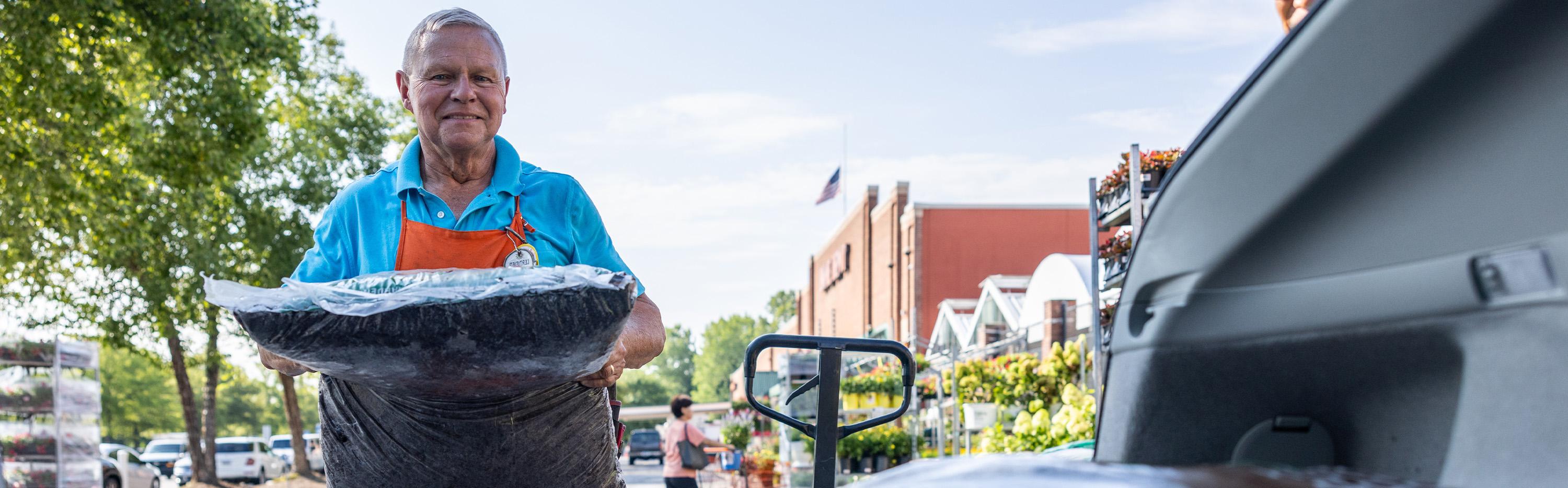 A Home Depot associate standing outside of the garden center with a bag of mulch