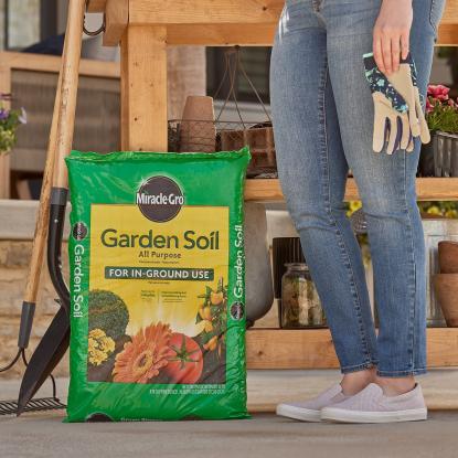 A woman standing next to a bag of garden soil holding gloves