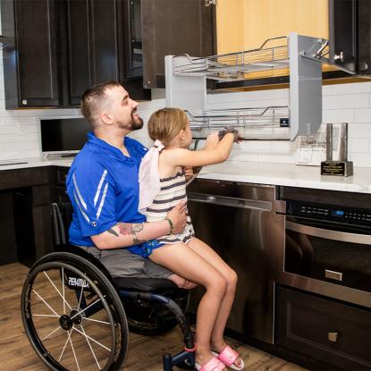 A veteran in a wheelchair with his daughter on his lap, looking at their new kitchen cabinet